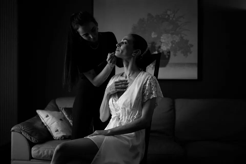 Foto in bianco e nero della sposa in vestaglia di pizzo durante il trucco.