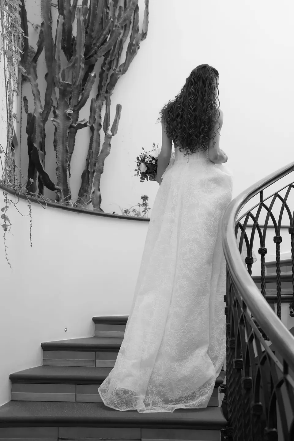Black and white photo of the bride from behind at the top of the staircase.