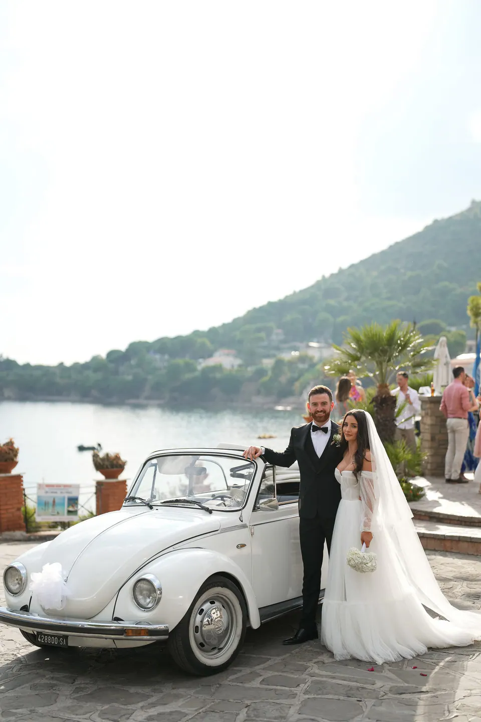 Das Brautpaar neben einem weißen VW-Käfer-Cabrio, dahinter die Küste des Cilento und das Meer.