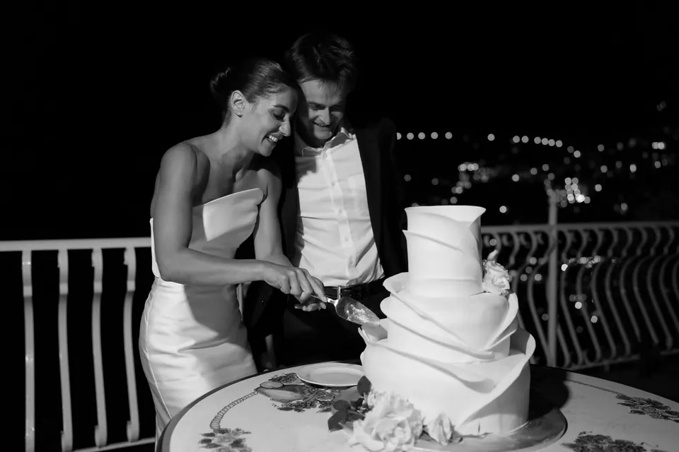 Black and white photo of the couple cutting the cake at night.