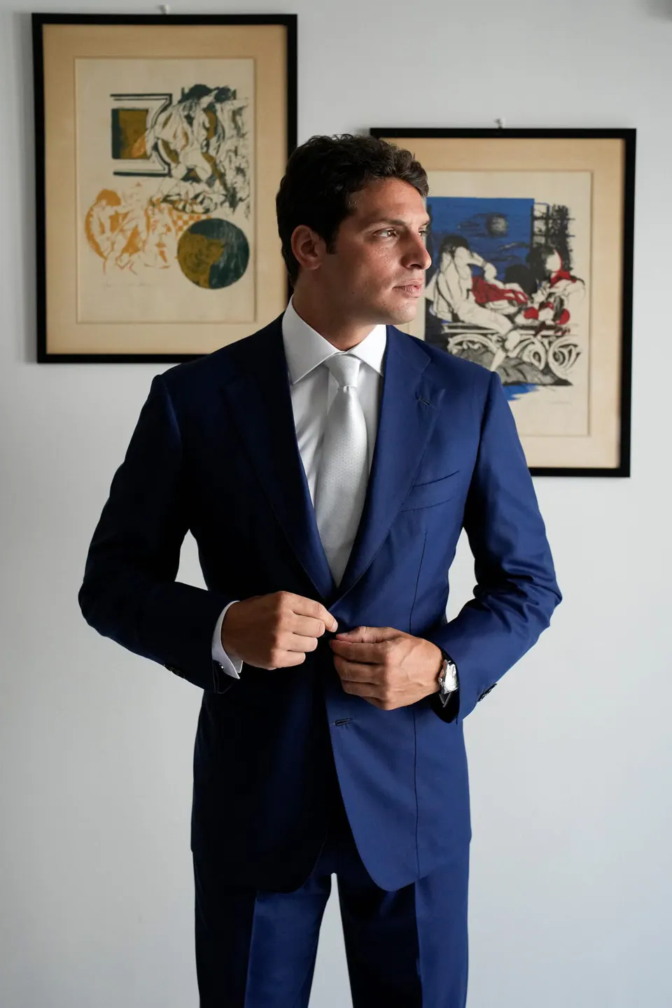 Lo sposo abbottona la giacca blu sotto stampe incorniciate.