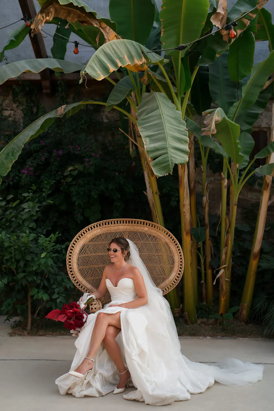Sposa seduta su una poltrona in vimini a pavone sotto i banani al Castello di Rocca Cilento.