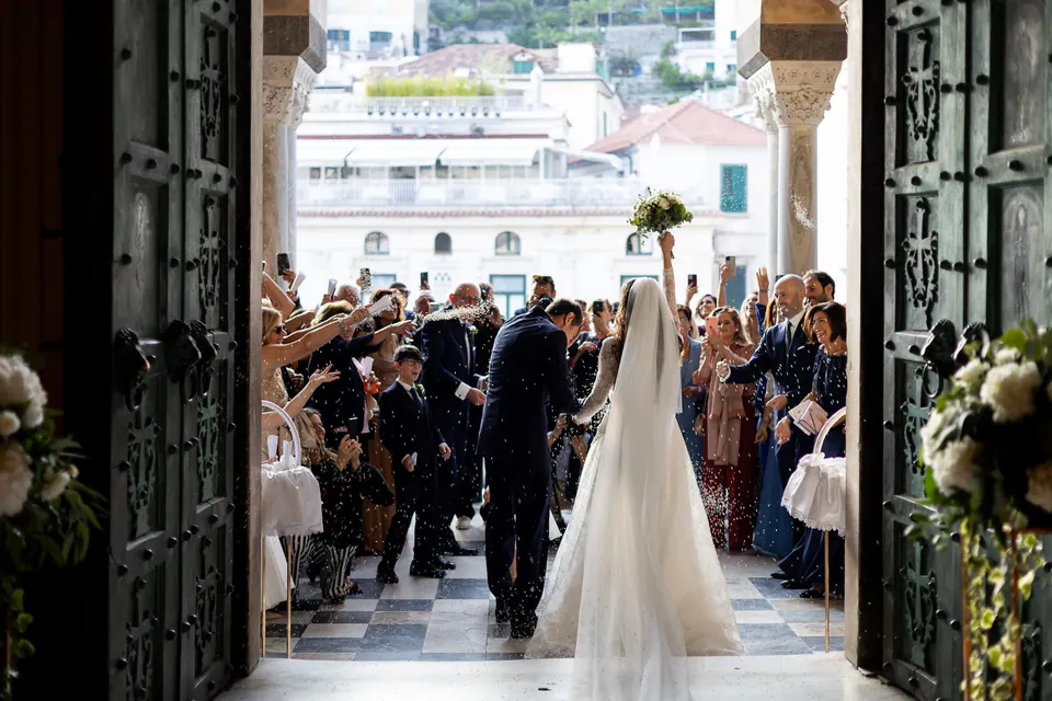 Bride and groom walking out through the cathedral doors into the crowd.