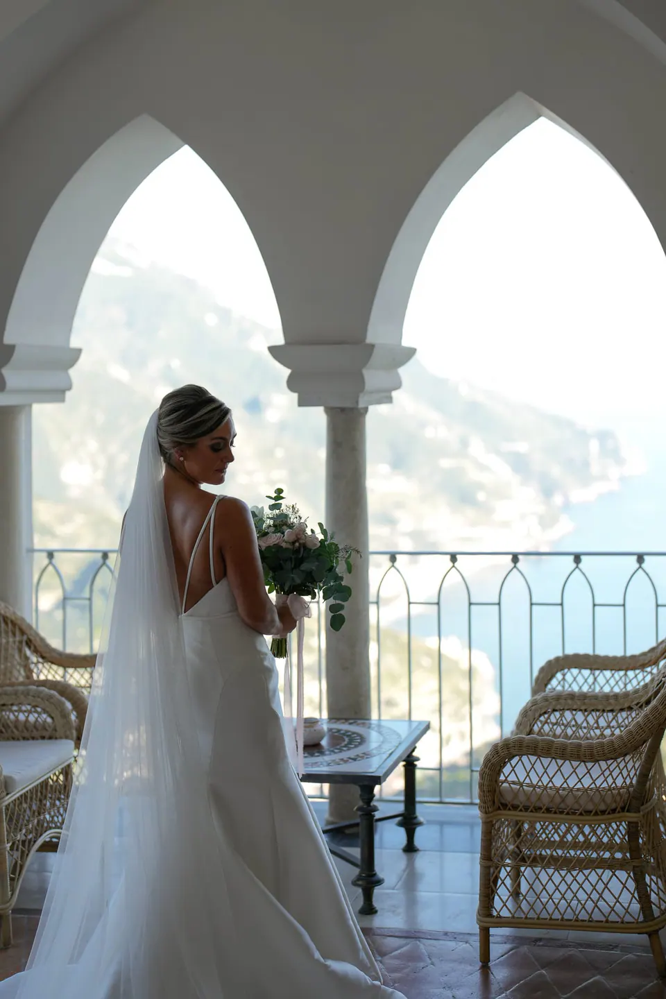 Bride under the white arches of the Belmond Hotel Caruso, the Amalfi Coast behind her