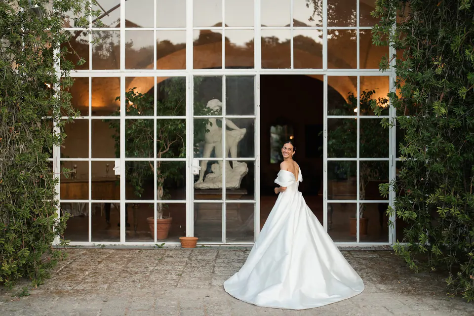 Sposa davanti alle vetrate dell'orangerie di Torre San Severino, tra piante rampicanti.