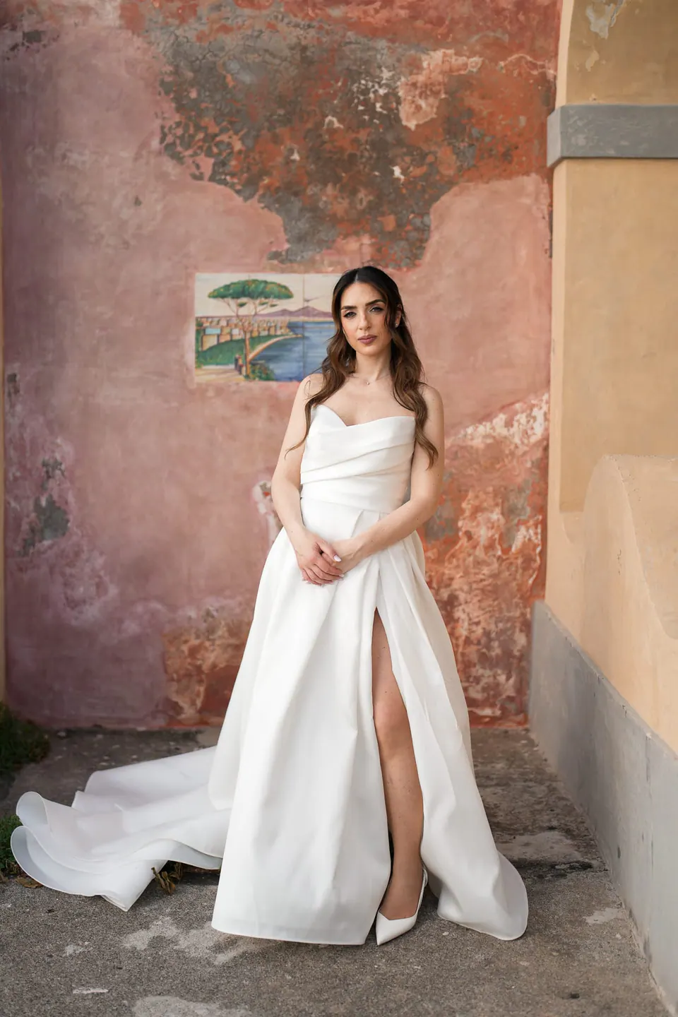 La novia con vestido palabra de honor junto a una pared rosa desgastada.
