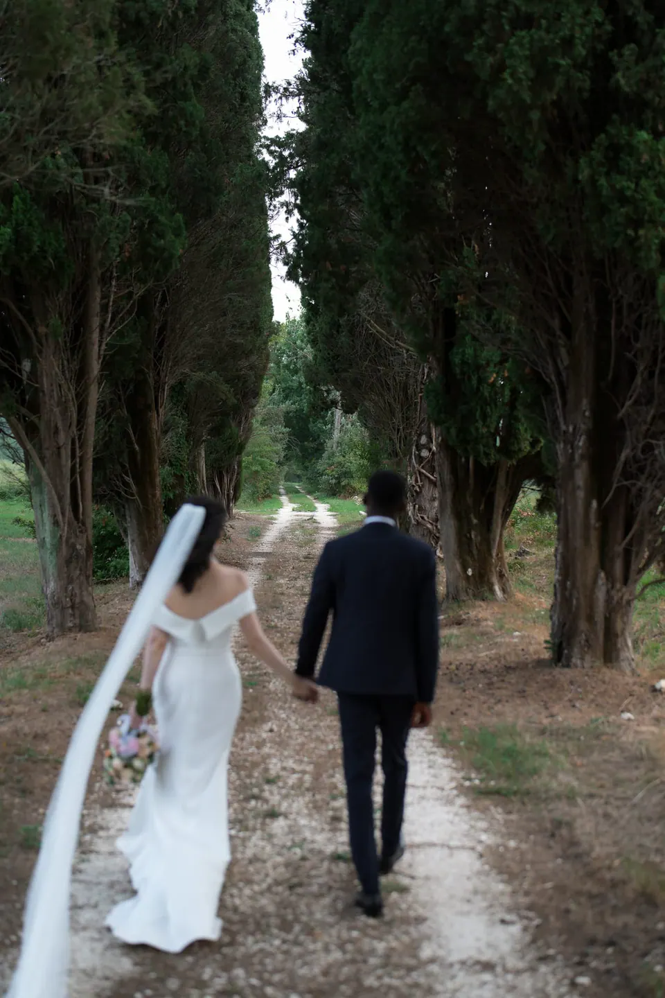 La pareja se aleja por un camino de cipreses, con el velo arrastrando, en los jardines de Villa Ortensia D’Avalos.