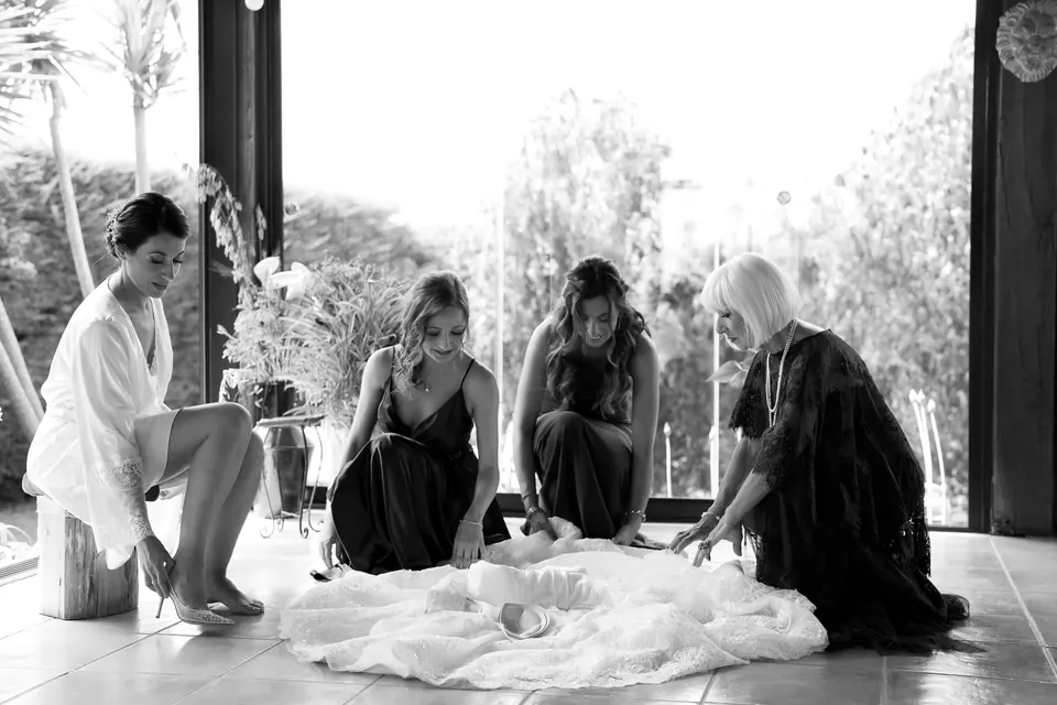 Black and white photo of women arranging the bride's dress under the pergola