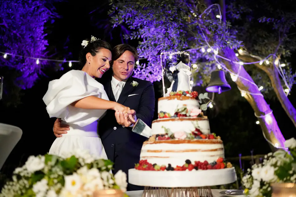 Bride and groom cutting their wedding cake in the garden under purple lights.