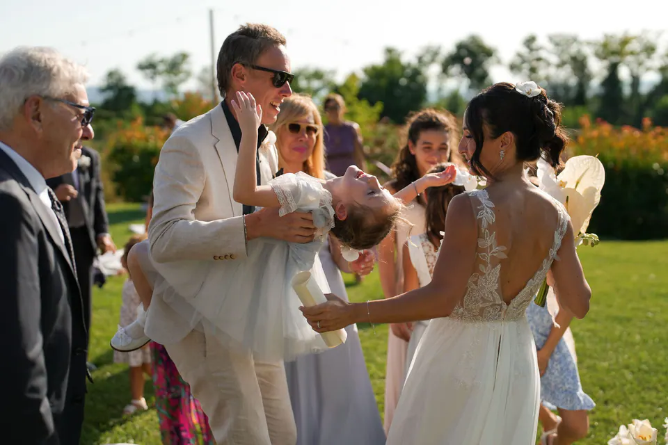 The groom playing with a little girl among the guests, the bride laughing beside him.