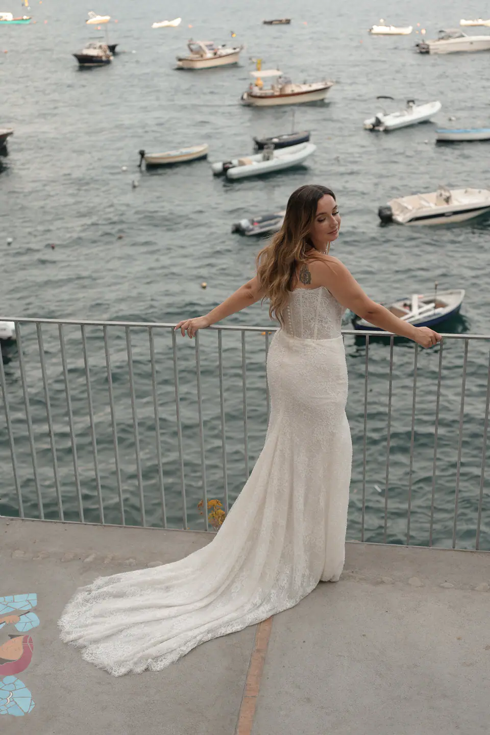 Bride leaning on a railing above the harbour, boats moored below.