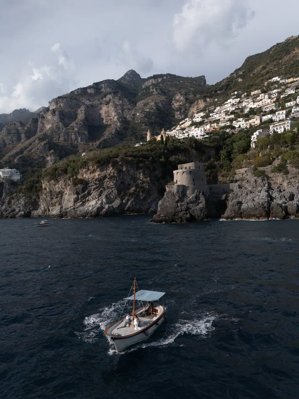 A wooden boat crossing the deep blue sea below the cliffs near Positano.