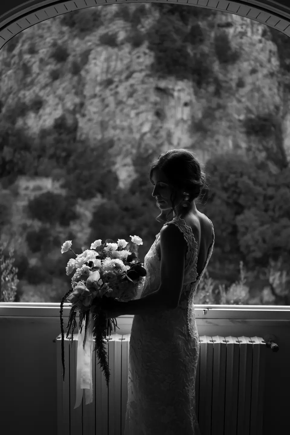Black and white silhouette of the bride with her bouquet at a window.