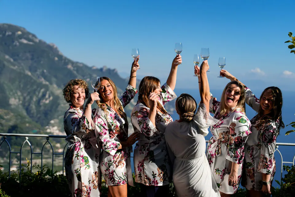 Bridesmaids in floral robes raising their glasses on a terrace above the Amalfi Coast