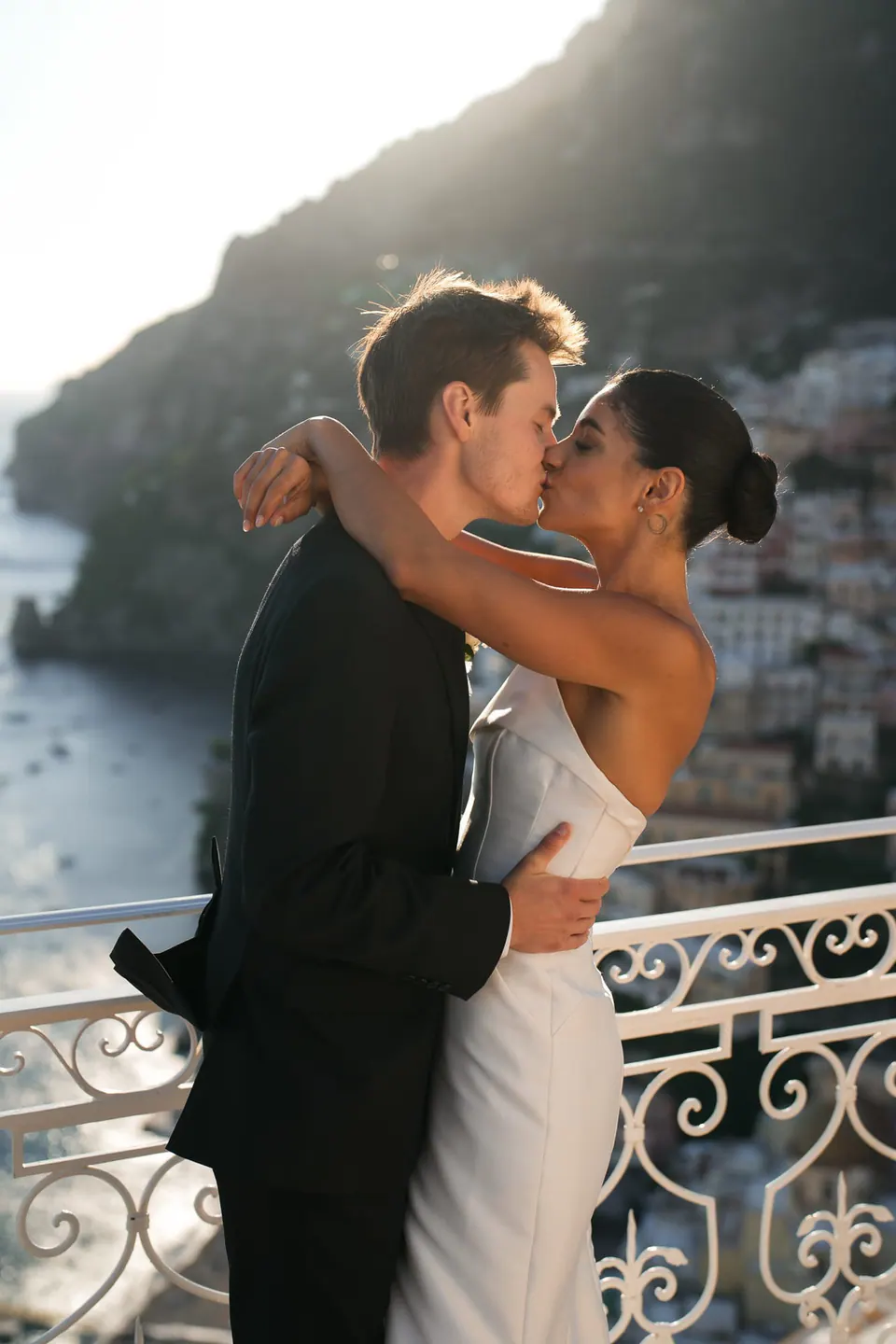 Bride and groom embracing at the wrought-iron railing above Positano.
