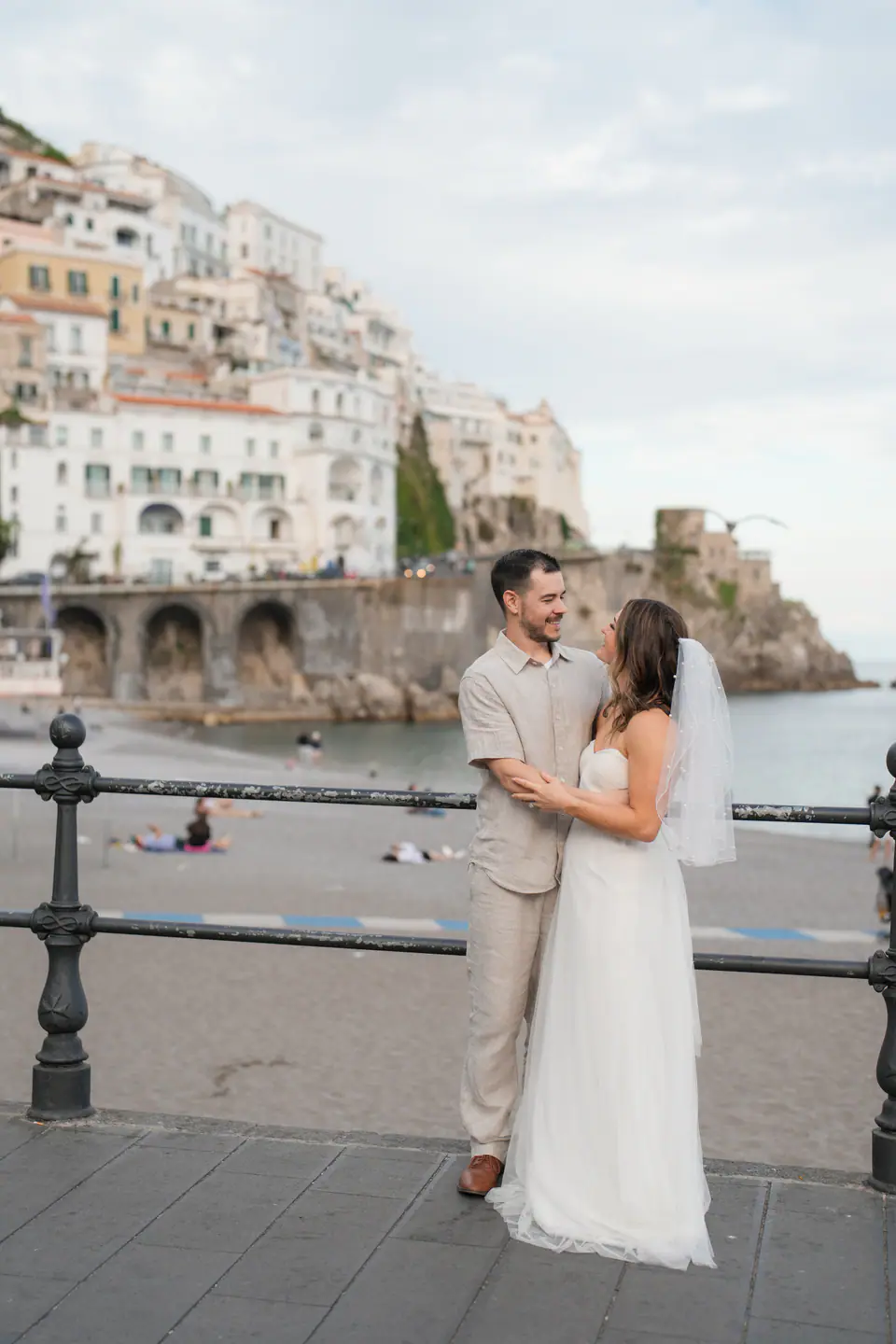 Couple at the seafront railing, the coast of Amalfi stretching behind them.