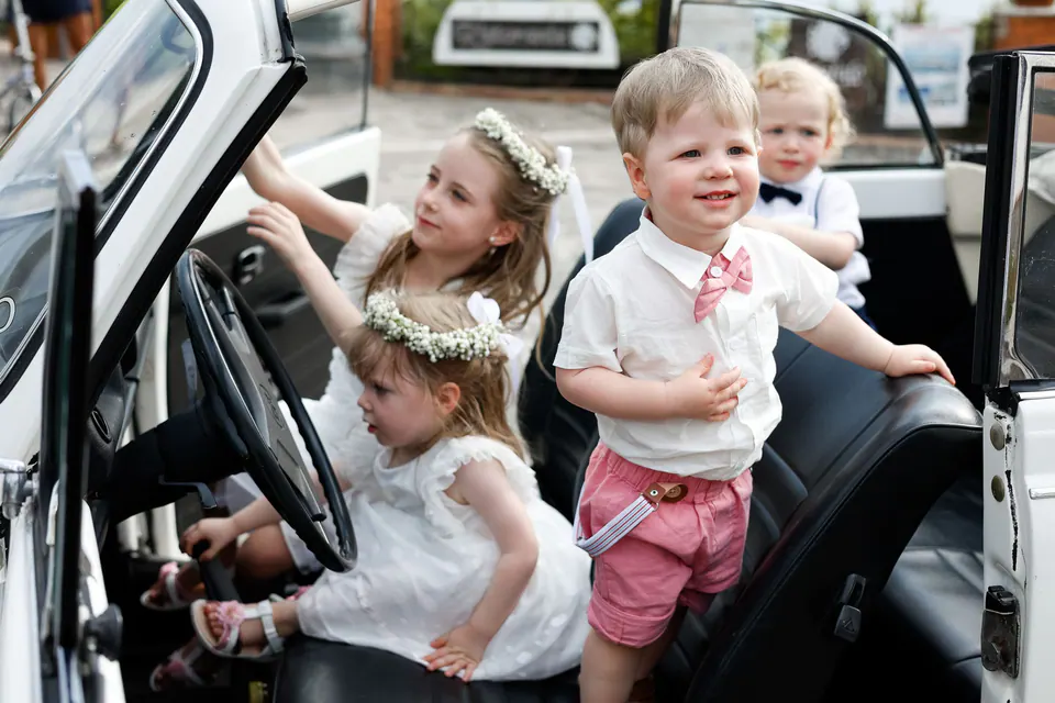 Kinder spielen im weißen Käfer-Cabrio, ein fröhlicher, spontaner Moment.
