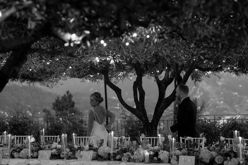 Black and white photo of the ceremony set in the garden under a tree, the coast beyond