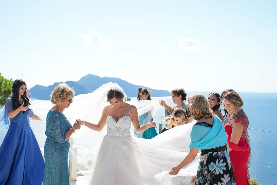 La mamma e le parenti sistemano l'abito della sposa in terrazza, Capri alle spalle.