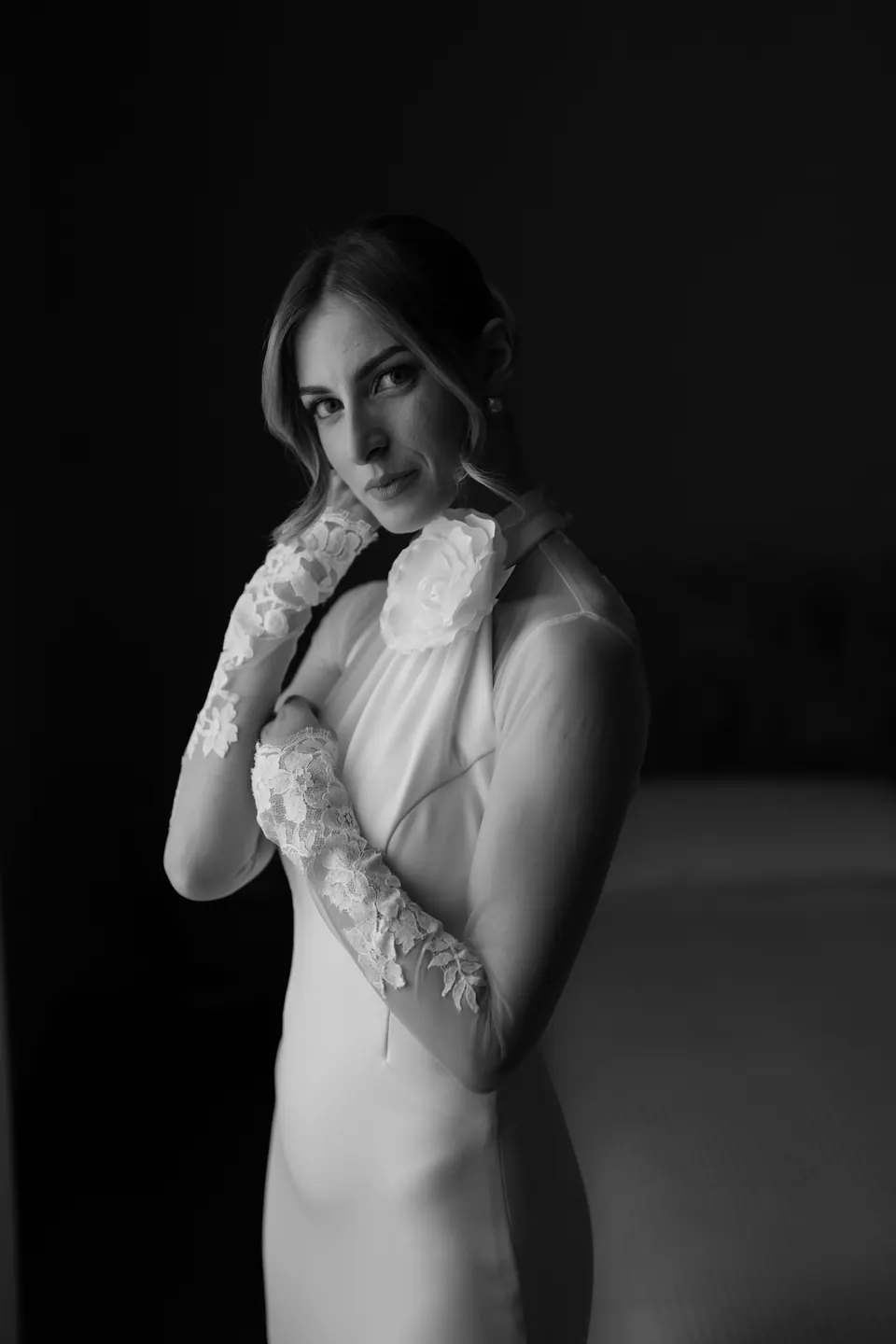 Ritratto in bianco e nero della sposa con l'abito dalle maniche di pizzo su fondo scuro.