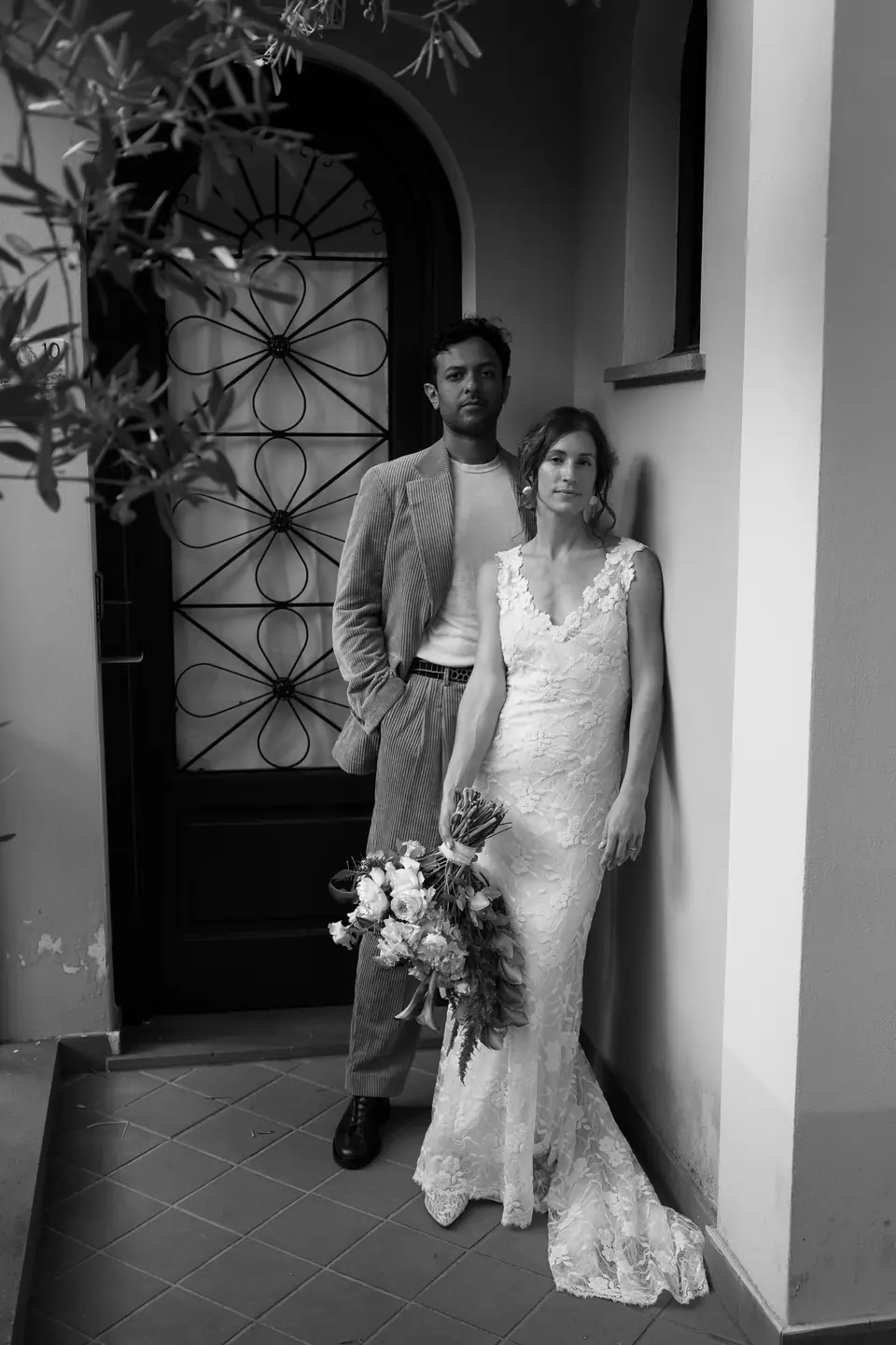 Black and white photo of the couple at a wrought-iron door, her large bouquet in her arms.