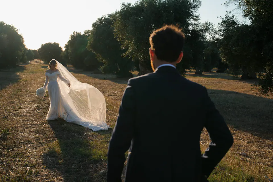 El novio mira a la novia en el olivar, con el velo al viento.