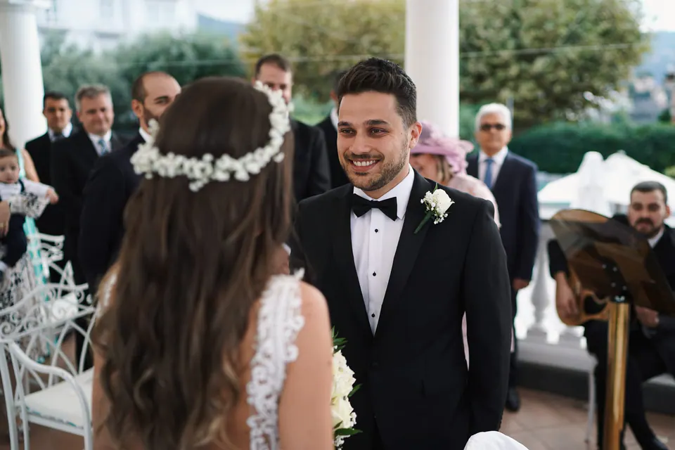 Groom smiling at the bride during the ceremony, guests behind them.