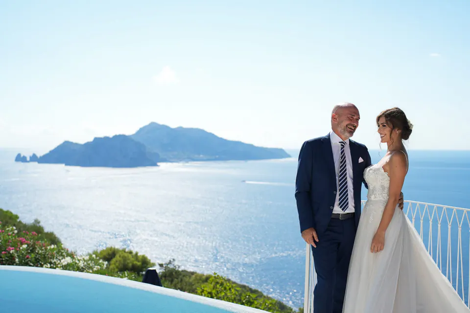 Gli sposi in posa sulla terrazza con una vista panoramica sul mare alle spalle.