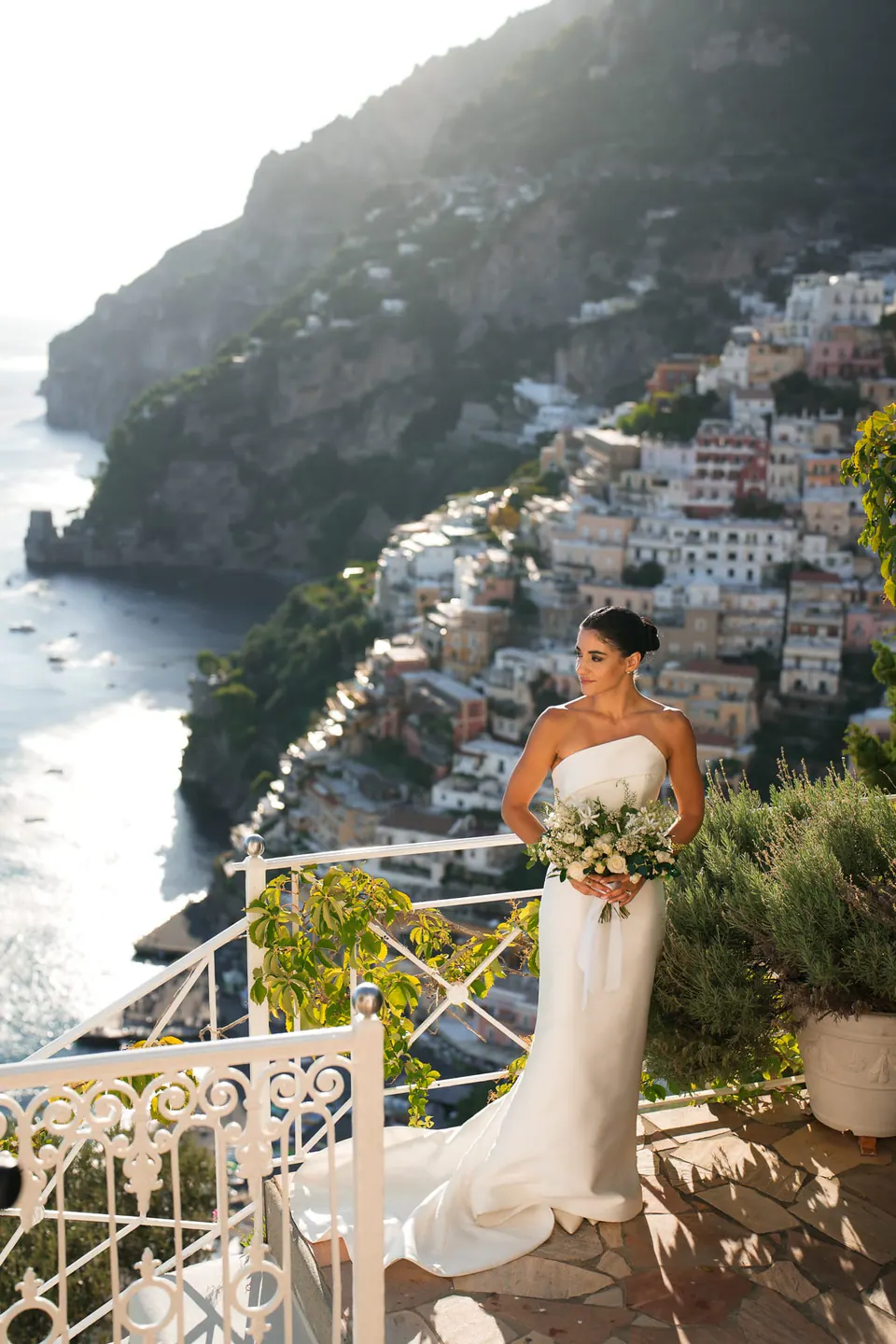 Bride standing on the terrace with her bouquet, the town and sea below.
