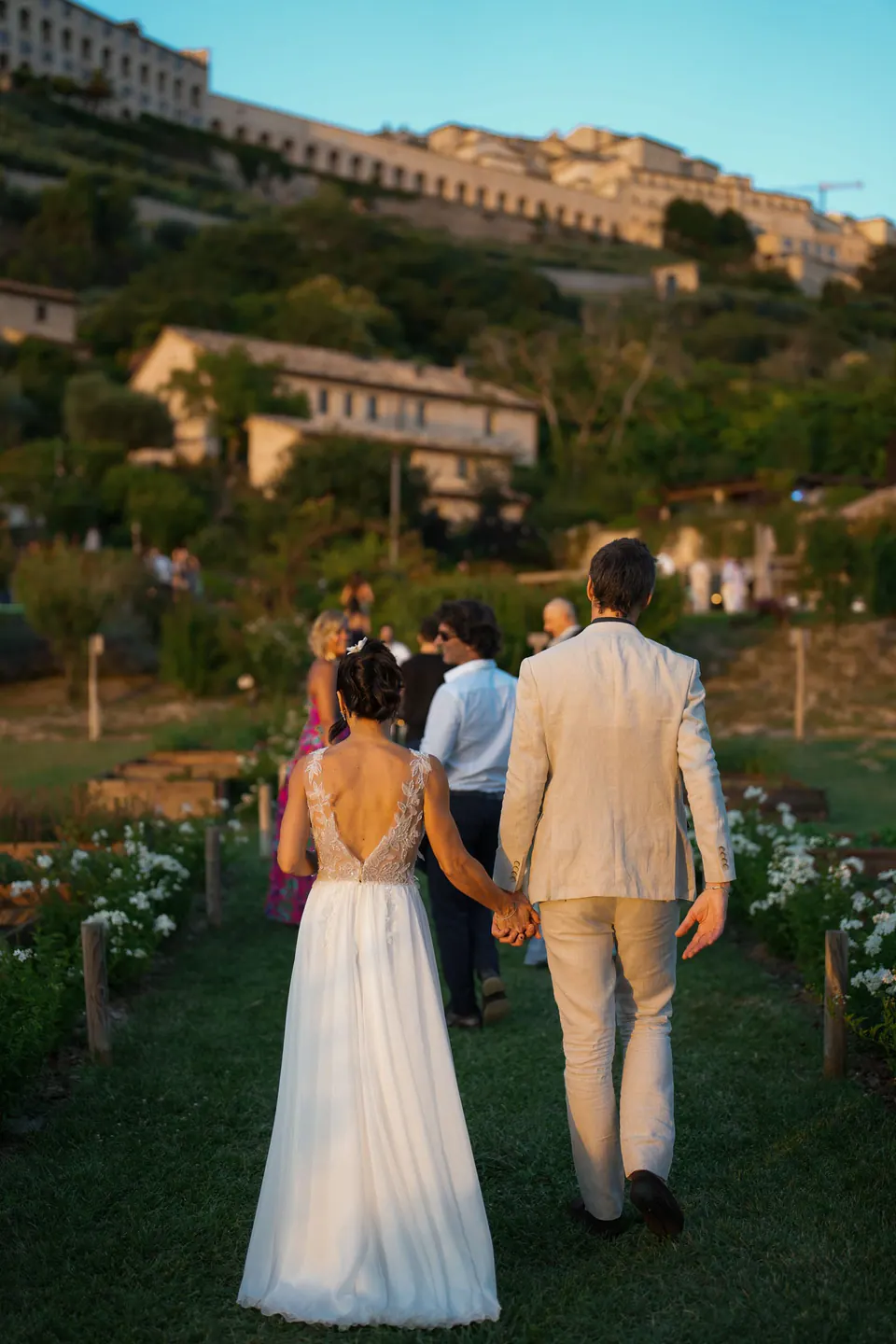 Bride and groom walking hand in hand with Assisi on the hill behind