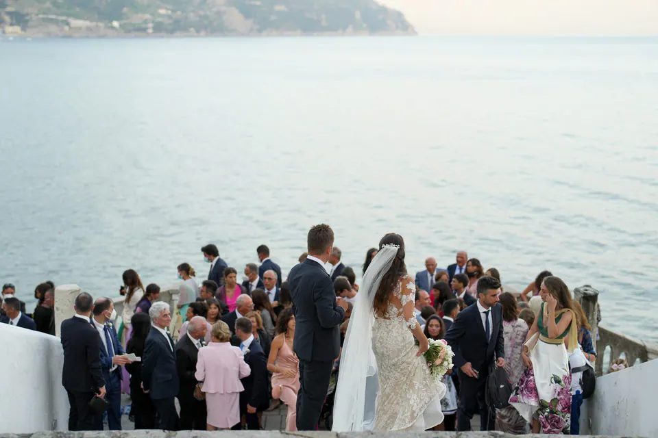 Braut und Gäste feiern auf der Terrasse, in der Ferne glitzert die Küste von Ravello.