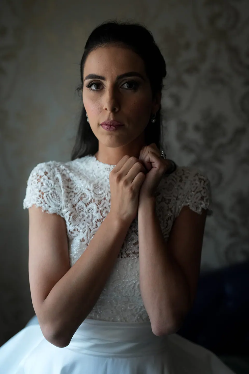 Bride with her hands at the lace collar of her dress, dark background