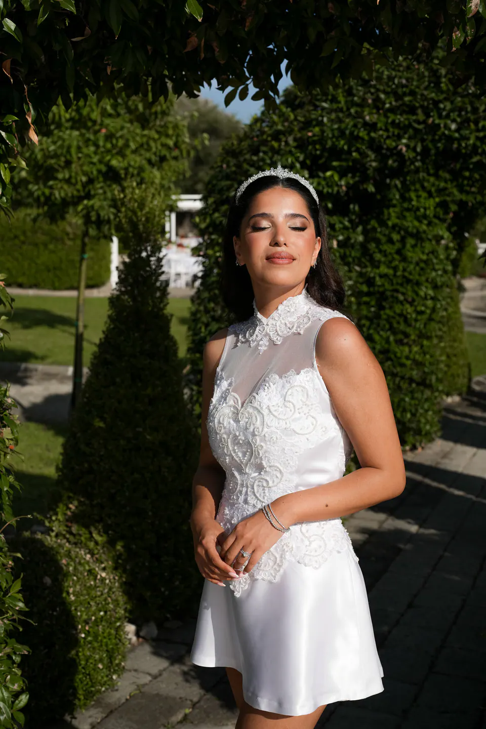 La mariée dans sa robe courte de fête entre les haies taillées du jardin, à l’heure dorée.