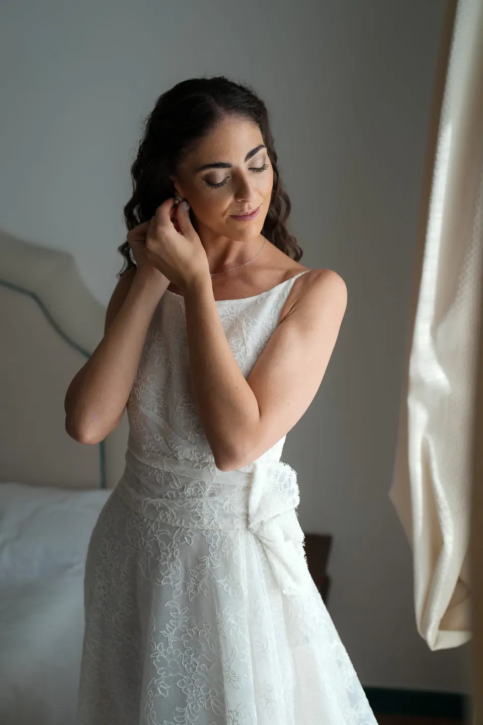 Bride putting on her earrings by the window.