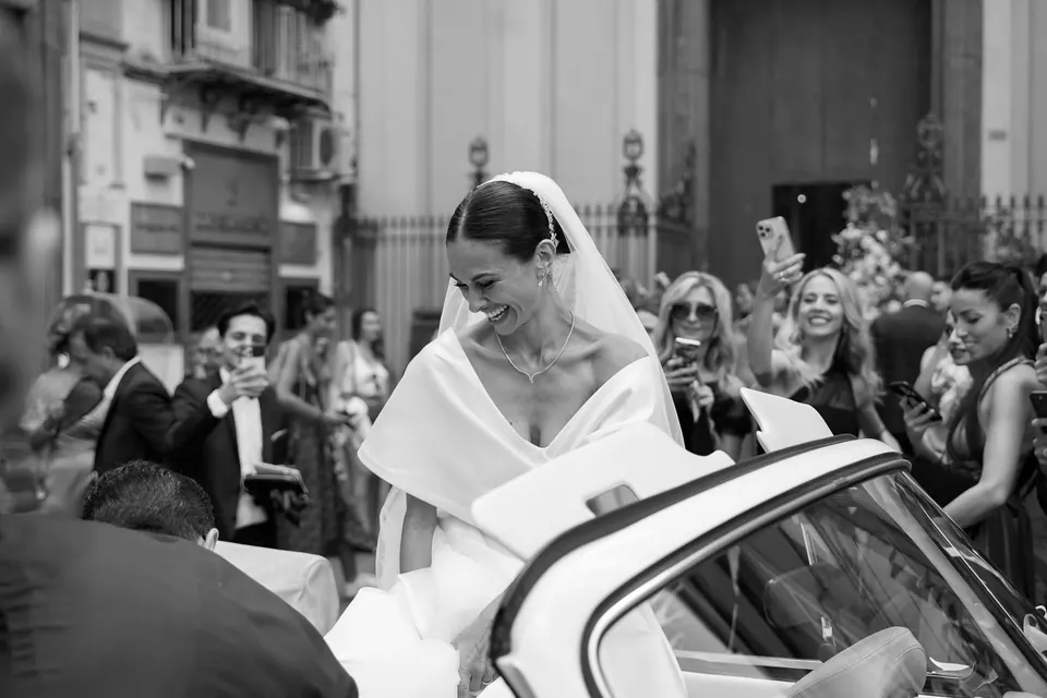 Foto in bianco e nero della sposa che scende dall'auto d'epoca davanti alla chiesa.