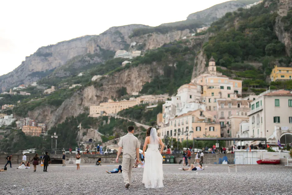 Wide view of the couple on the beach, Amalfi climbing the mountain behind them.