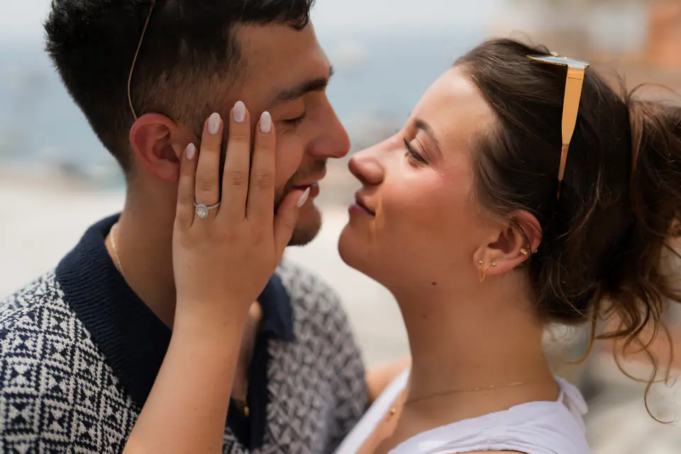 Close-up of her hand with the new ring on his face as they kiss.