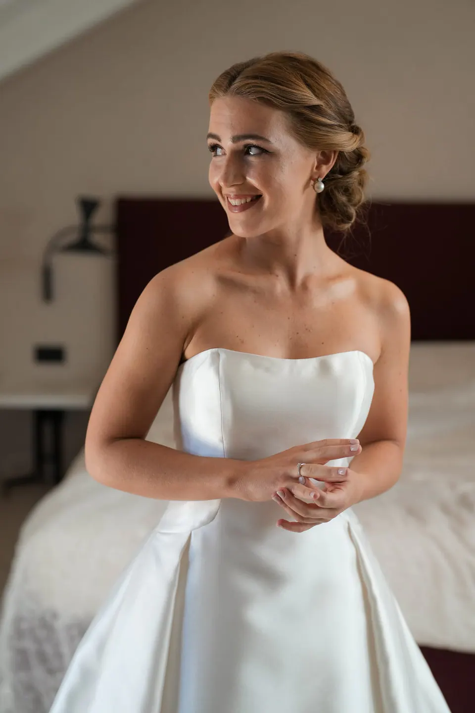 Die Braut lächelt im trägerlosen Kleid im Zimmer.