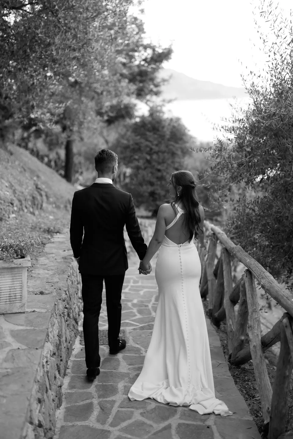 Bride and groom walking together through the villa gardens, soft sunset light on their faces.