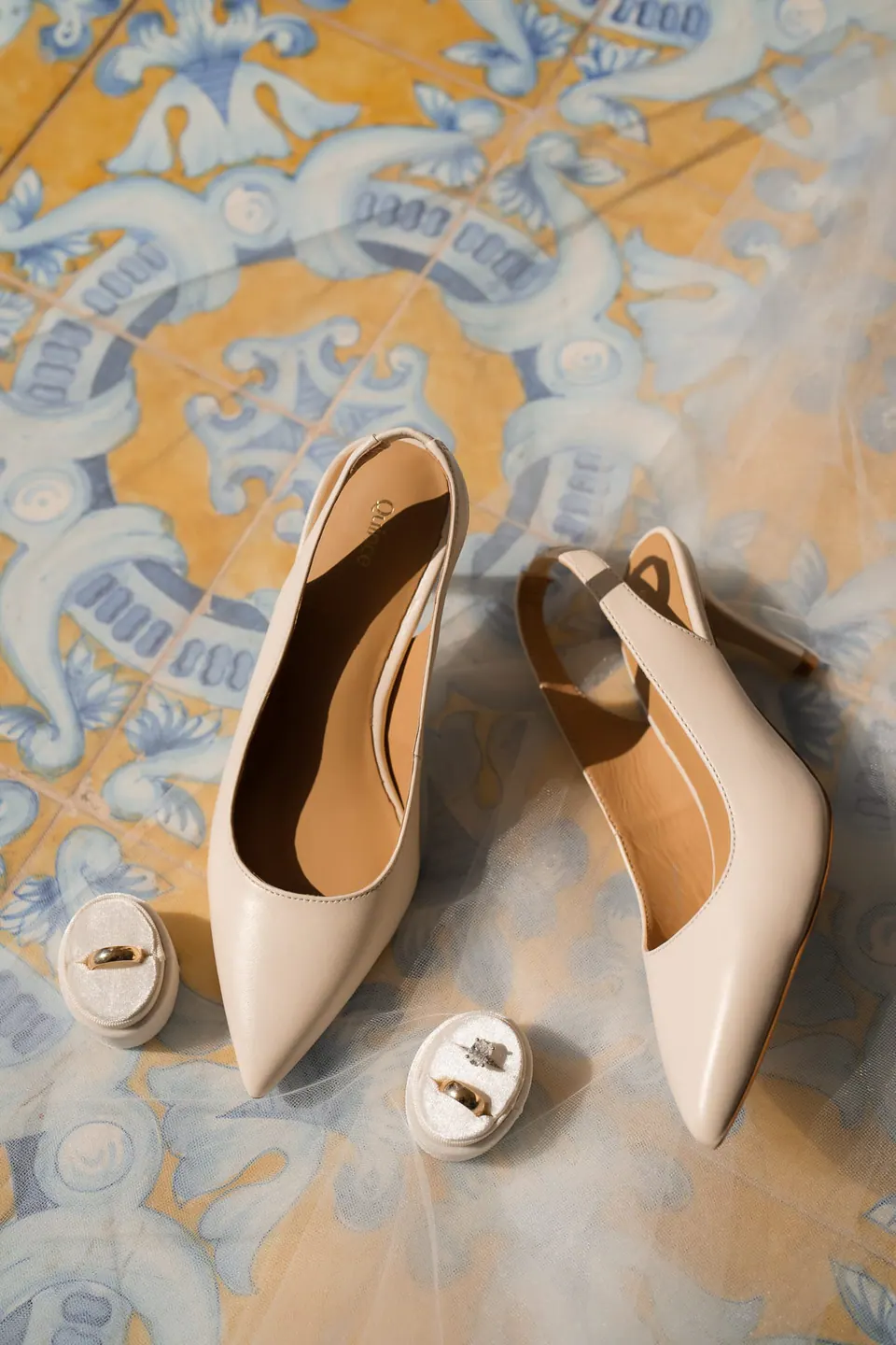 Ivory bridal heels and ring boxes on a yellow and blue majolica floor.