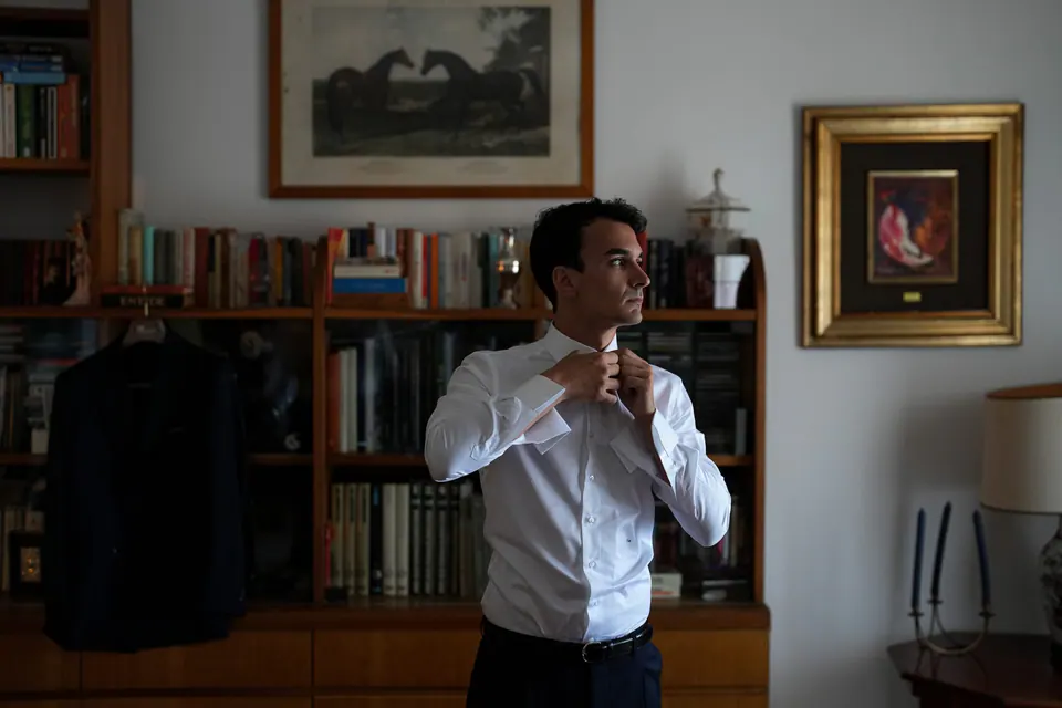 Groom adjusting his collar in a book-lined room