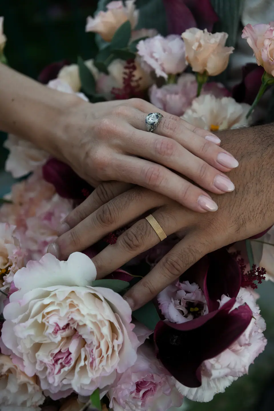 Close-up of their hands and rings on a bouquet of roses and peonies.