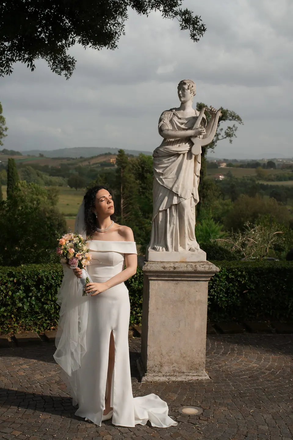 La novia con su ramo junto a una estatua clásica en el jardín, en Caserta.