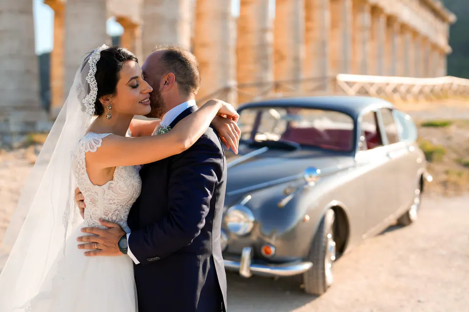 Bride and groom embracing beside a vintage car at Tenuta Cala Muletti.