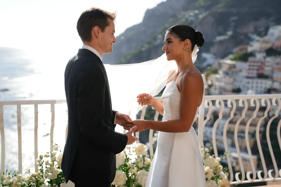 Bride and groom holding hands during their vows, Positano behind them.