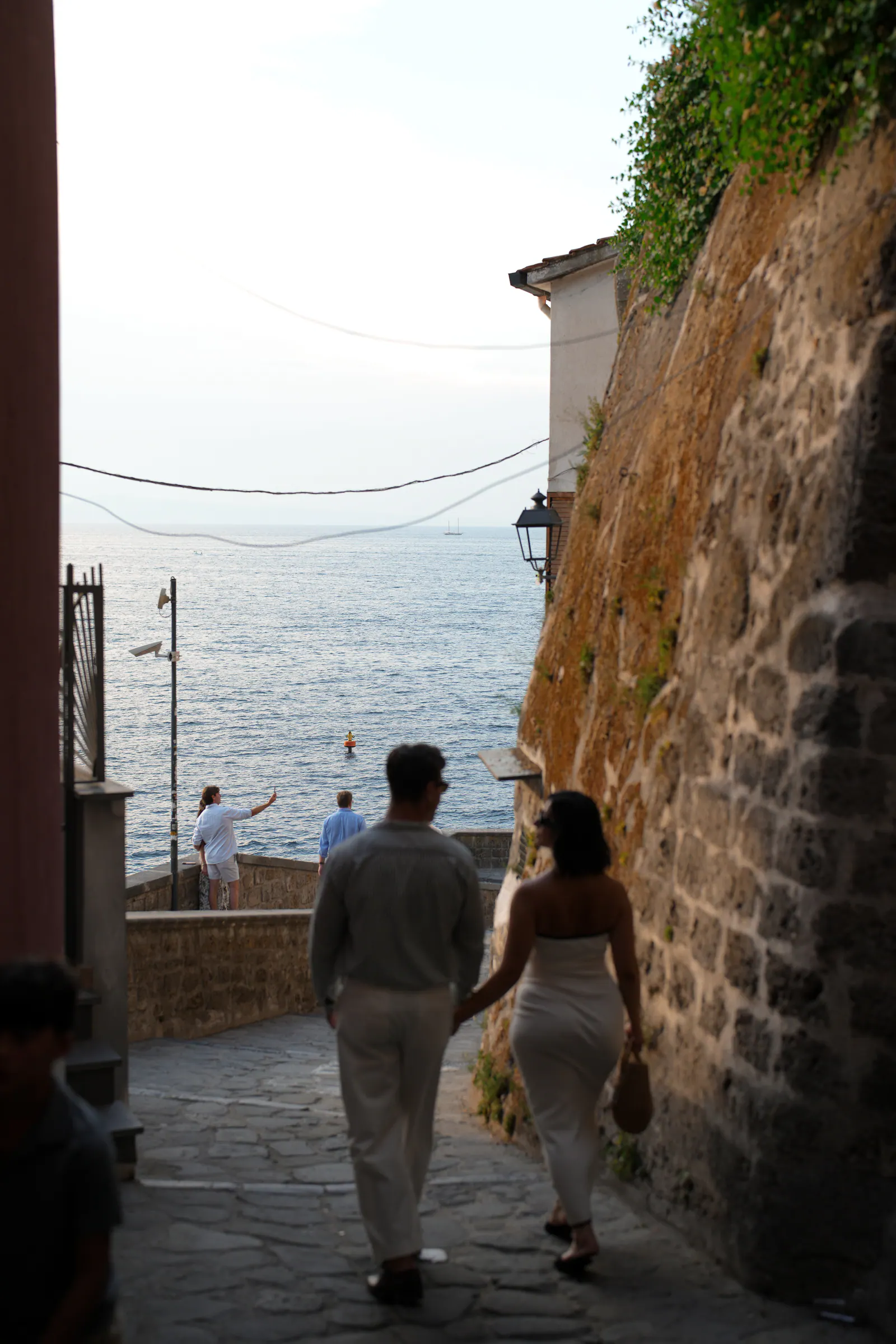 Couple walking down a narrow lane towards the sea in Sorrento.