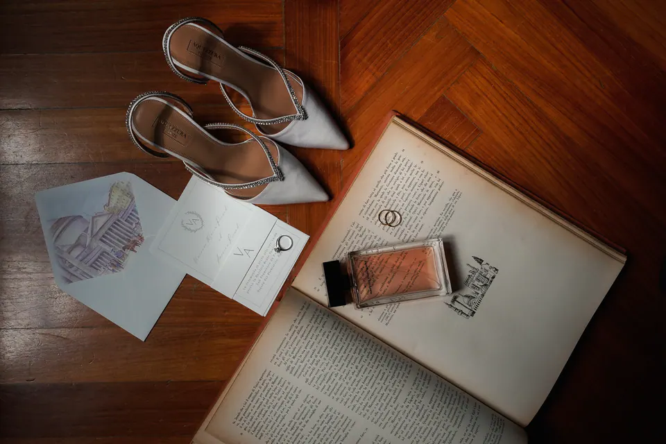Bridal shoes, invitations and perfume laid on an open book.