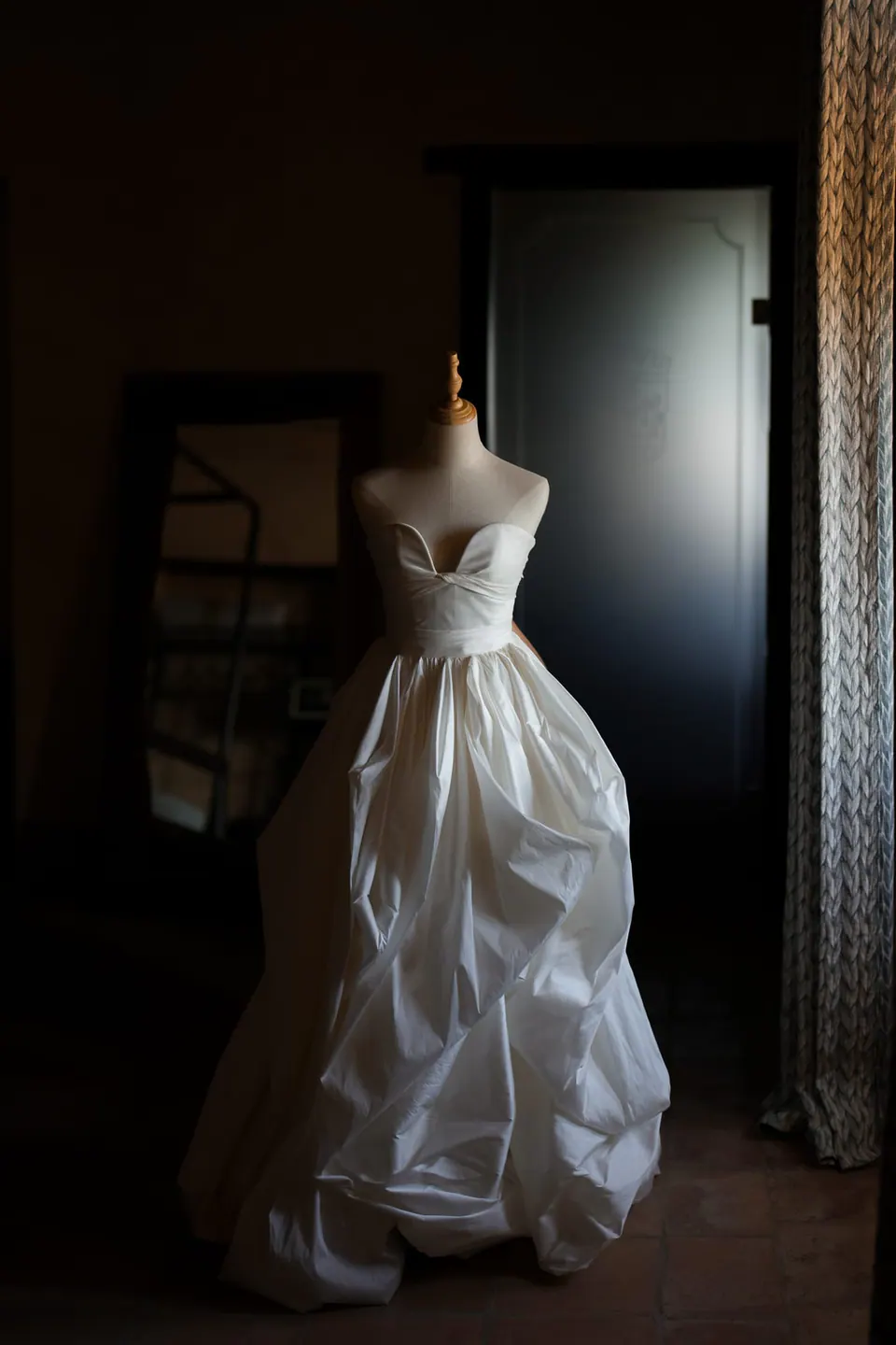 Abito da sposa su un manichino in una stanza in penombra del castello.