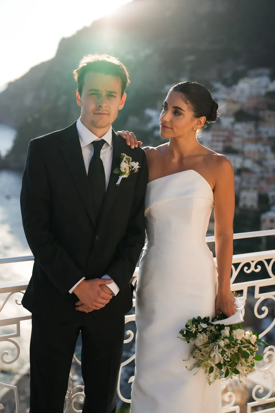 Bride and groom side by side on the terrace, bouquet in her hand.