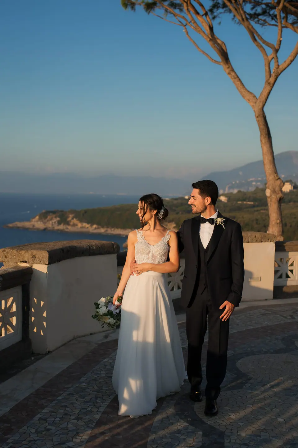 Bride and groom on the terrace at sunset, the coastline of the Sorrento peninsula behind them.